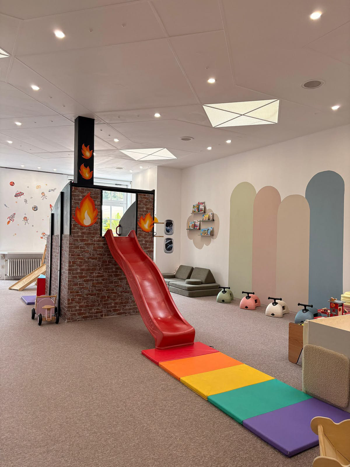 Heller Spielbereich bei Little Moon mit roter Rutsche und pastellfarbener Bögenwand